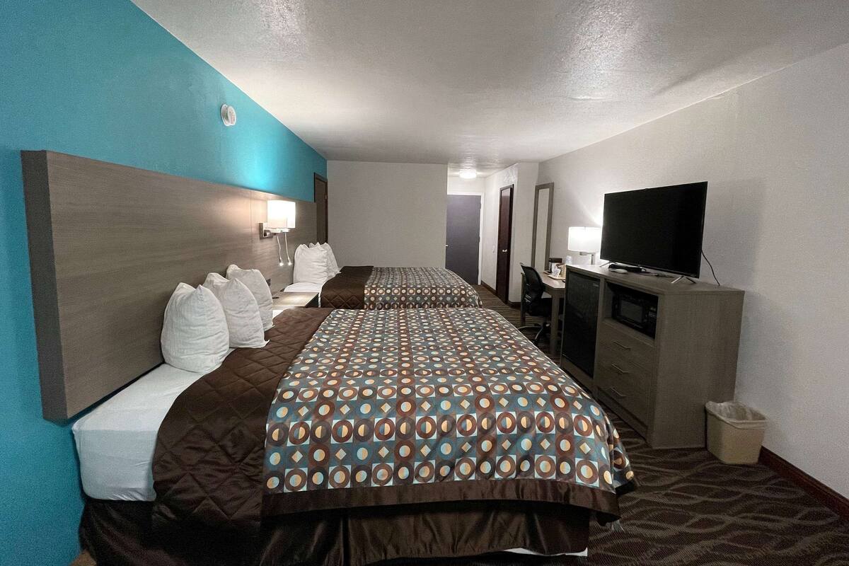 Ein Hotelzimmer mit zwei Betten, einem Fernseher, einem Schreibtisch und einer Mülleimer.