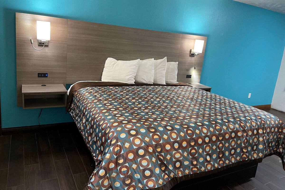 Ein Hotelzimmer mit einem hölzernen Kopfteil, einer gemusterten Bettdecke und einer blauen Akzentwand.