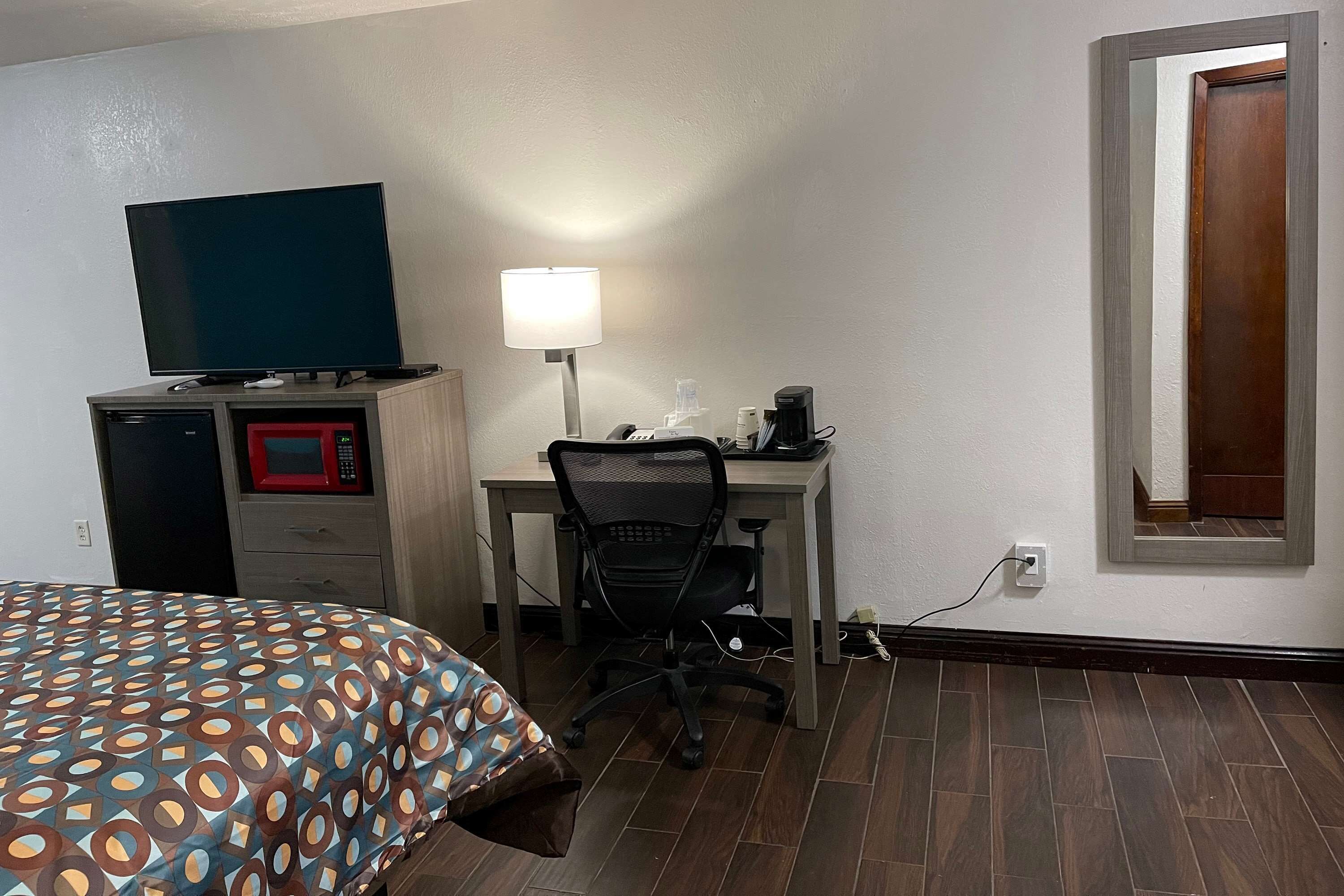 A hotel room with a bed, a desk with a computer, a TV, a lamp, and a microwave.