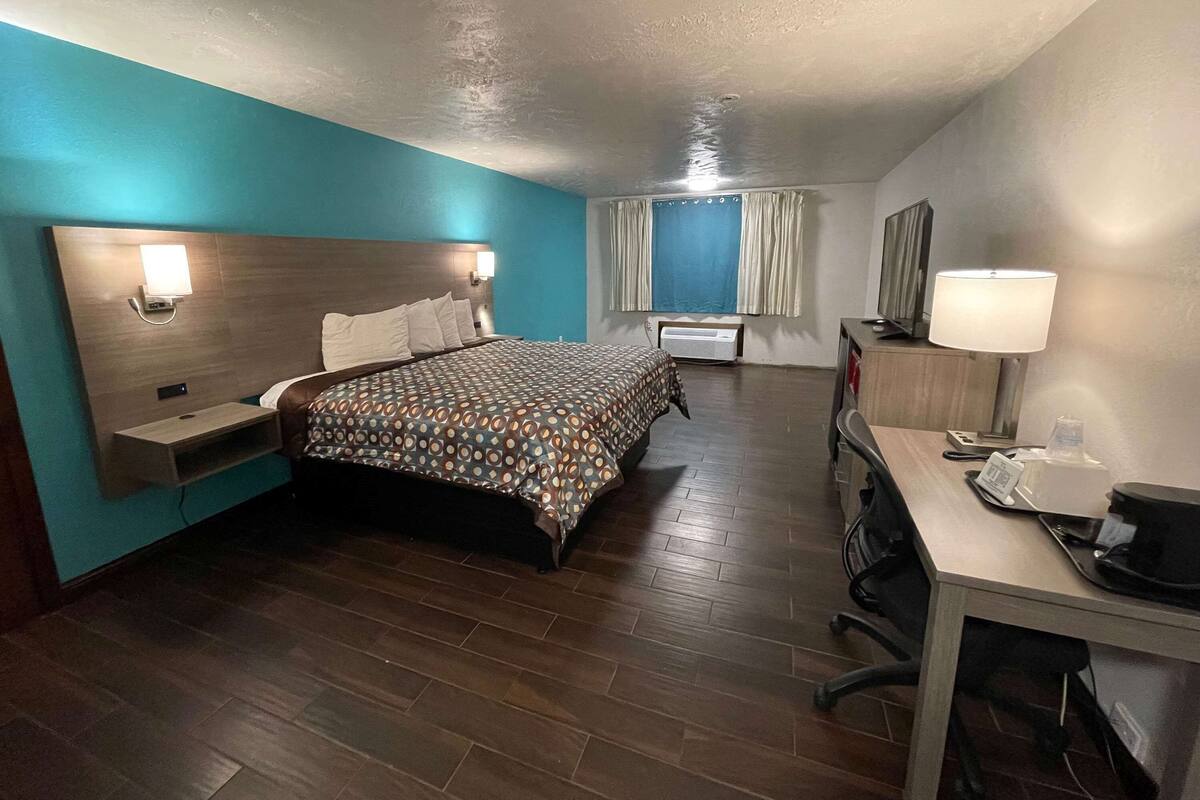 Ein Hotelzimmer mit Bett, Schreibtisch, Stuhl, Lampe und einem Fenster mit Vorhängen.