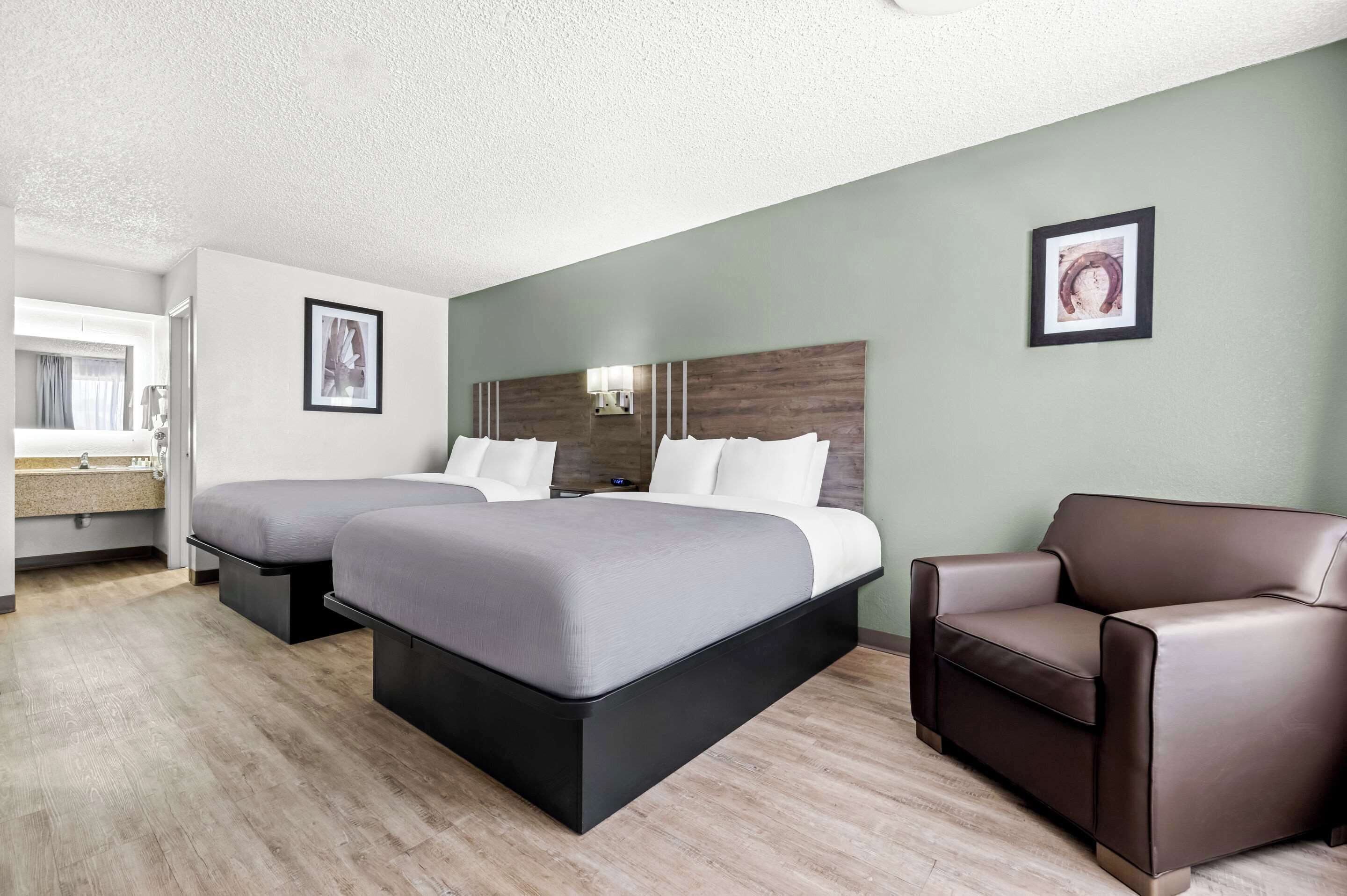 A hotel room with two beds, a sofa, a bathroom with a sink, and framed pictures on the walls.