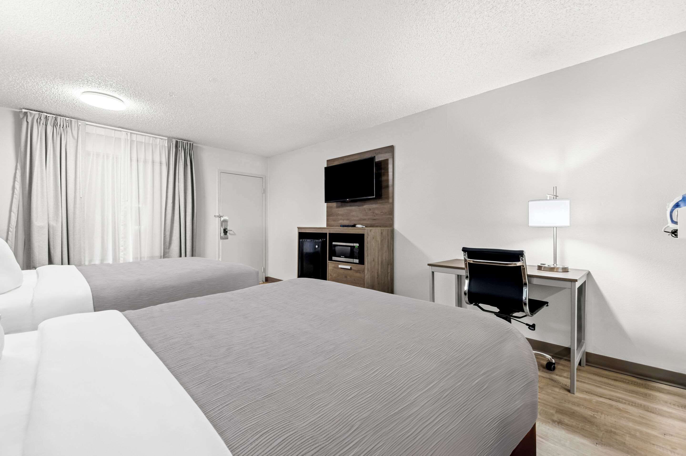 A hotel room with two beds, a desk with a chair, a flat-screen TV, a microwave, and a lamp.