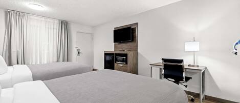 A hotel room with two beds, a desk with a chair, a flat-screen TV, a microwave, and a lamp.