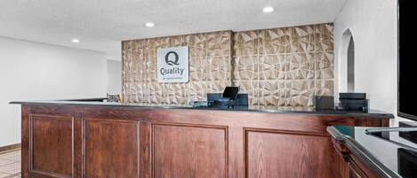 A reception desk with a 'Quality by Choice Hotels' sign, a wooden panel wall, and a tiled floor.