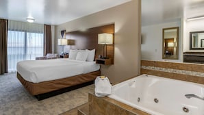 Una habitación de hotel con una cama grande, un baño con bañera y un espejo amplio.