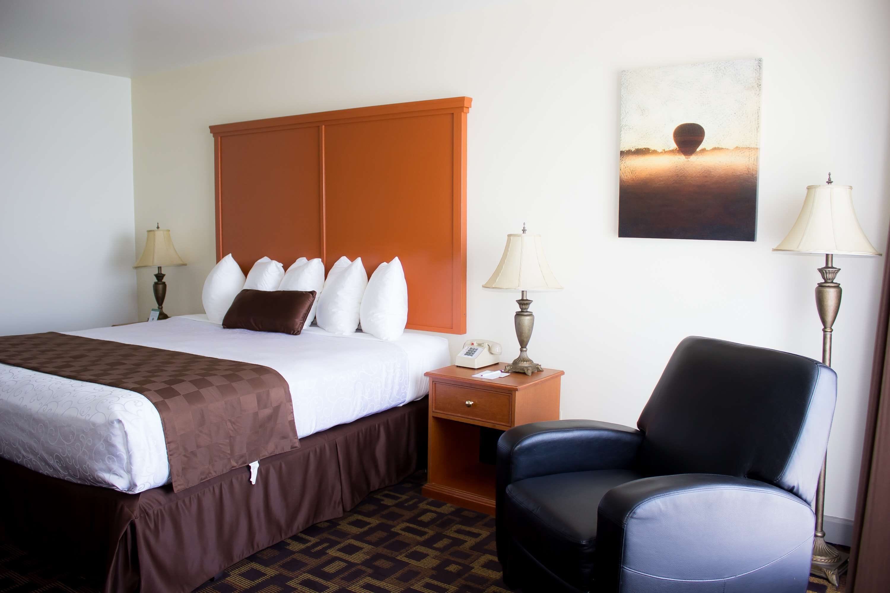 A hotel room with a bed, a nightstand, a chair, and a painting on the wall.