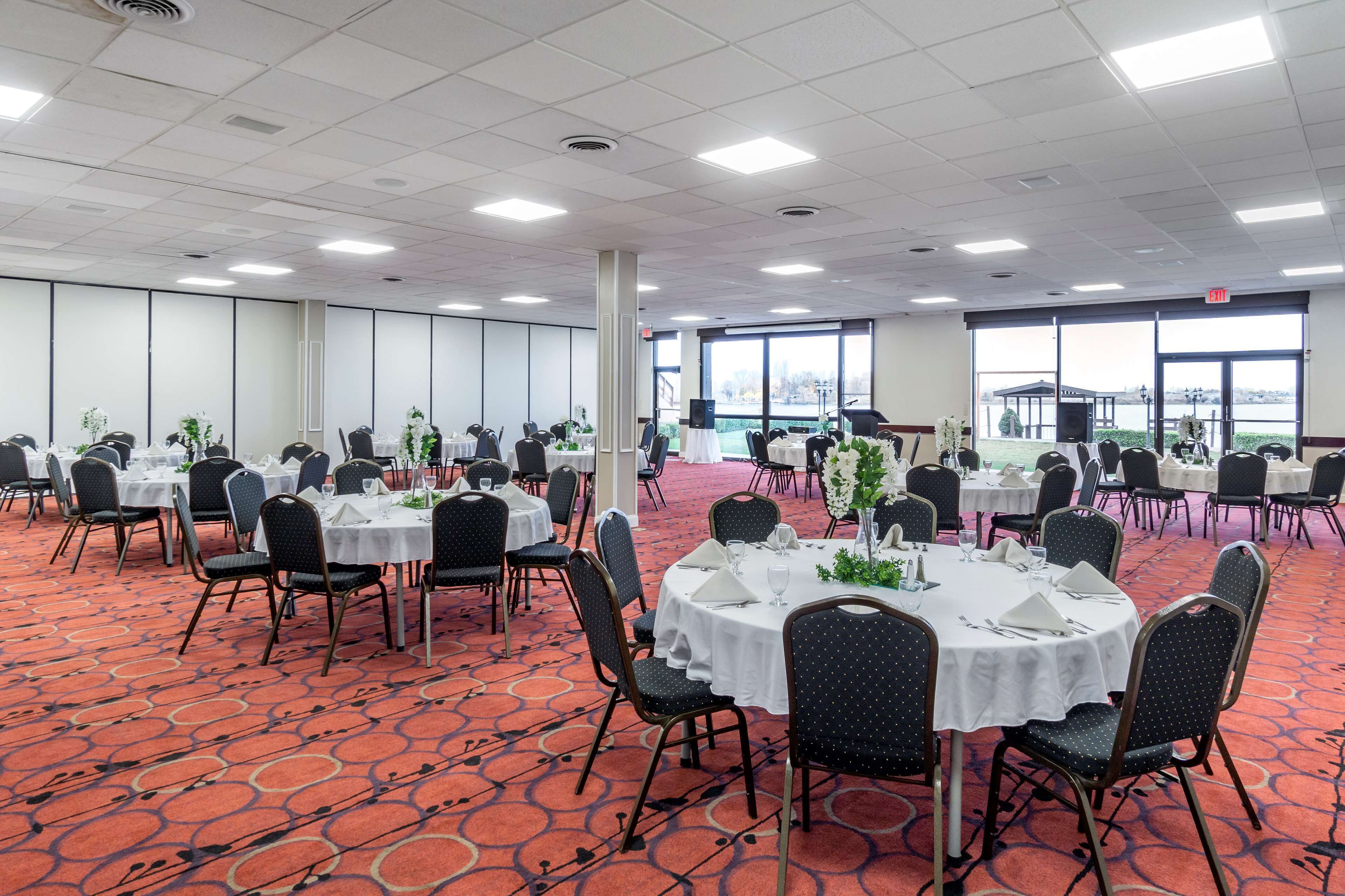 A banquet hall with round tables, chairs, and a red carpeted floor.