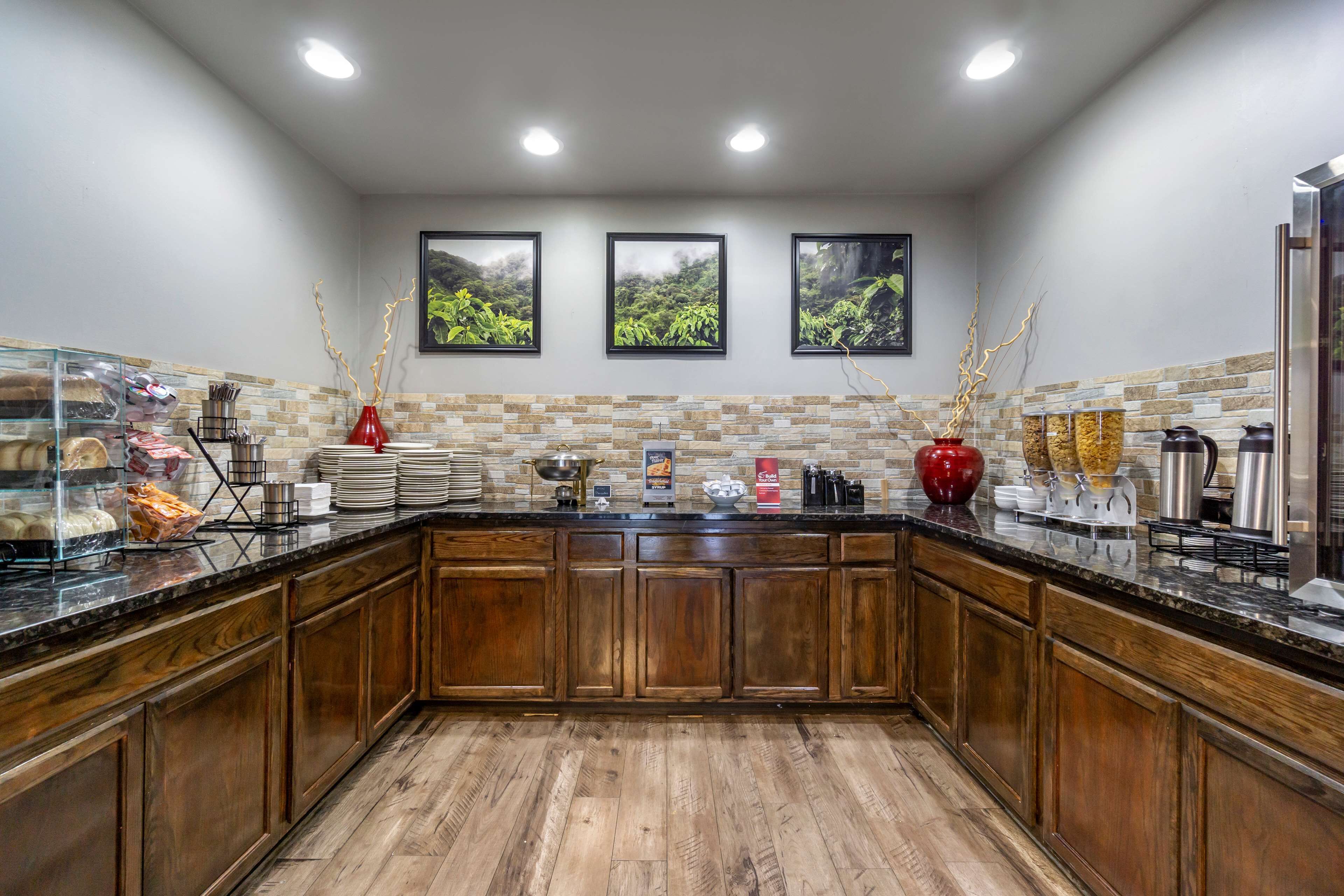 Cocina con armarios de madera, encimera de granito y salpicadero de piedra. Hay tres cuadros en la pared, una cafetera y un jarrón rojo.