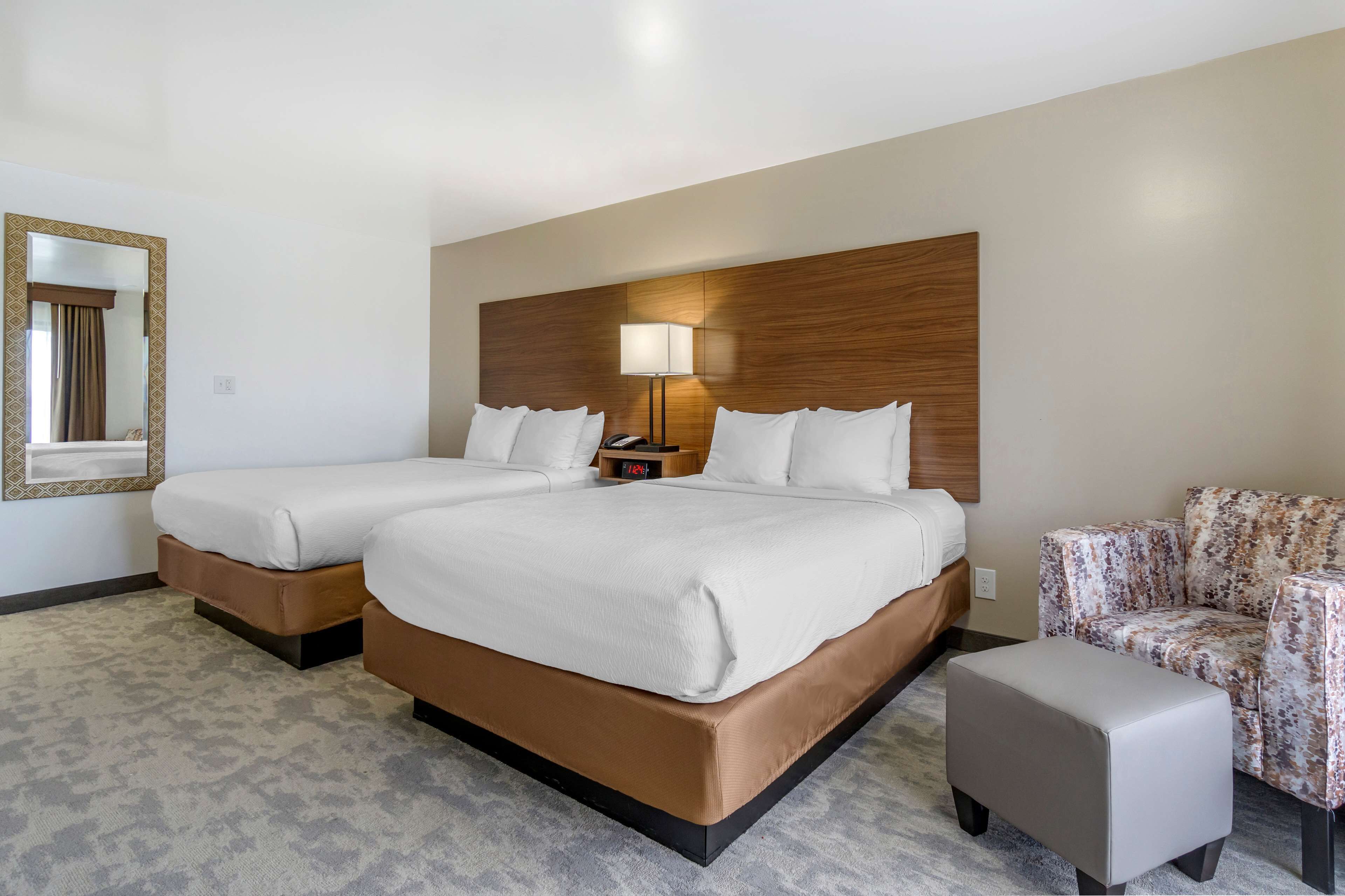 A hotel room with two beds, a sofa, a chair, a lamp, and a mirror.