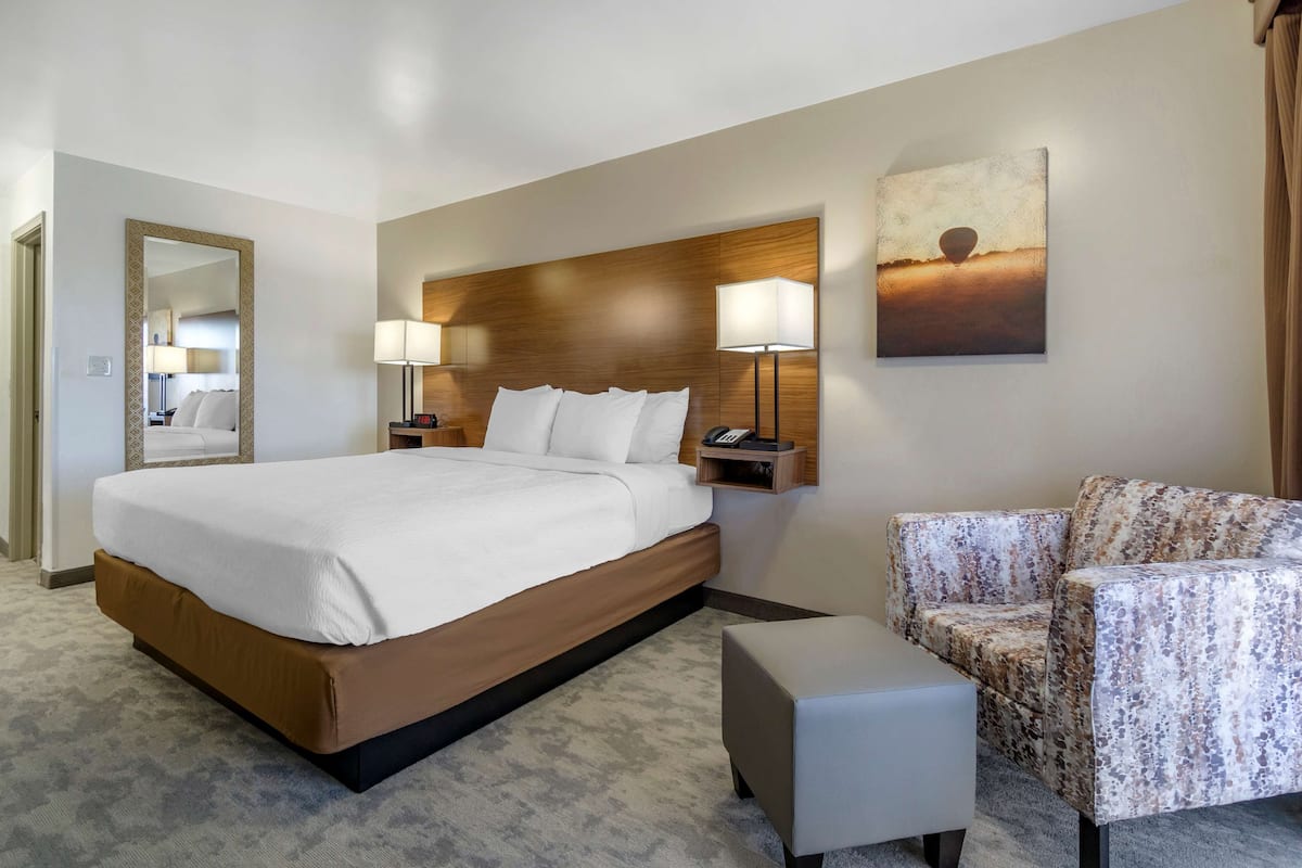 A hotel room with a large bed, two bedside lamps, a chair, and a small table.