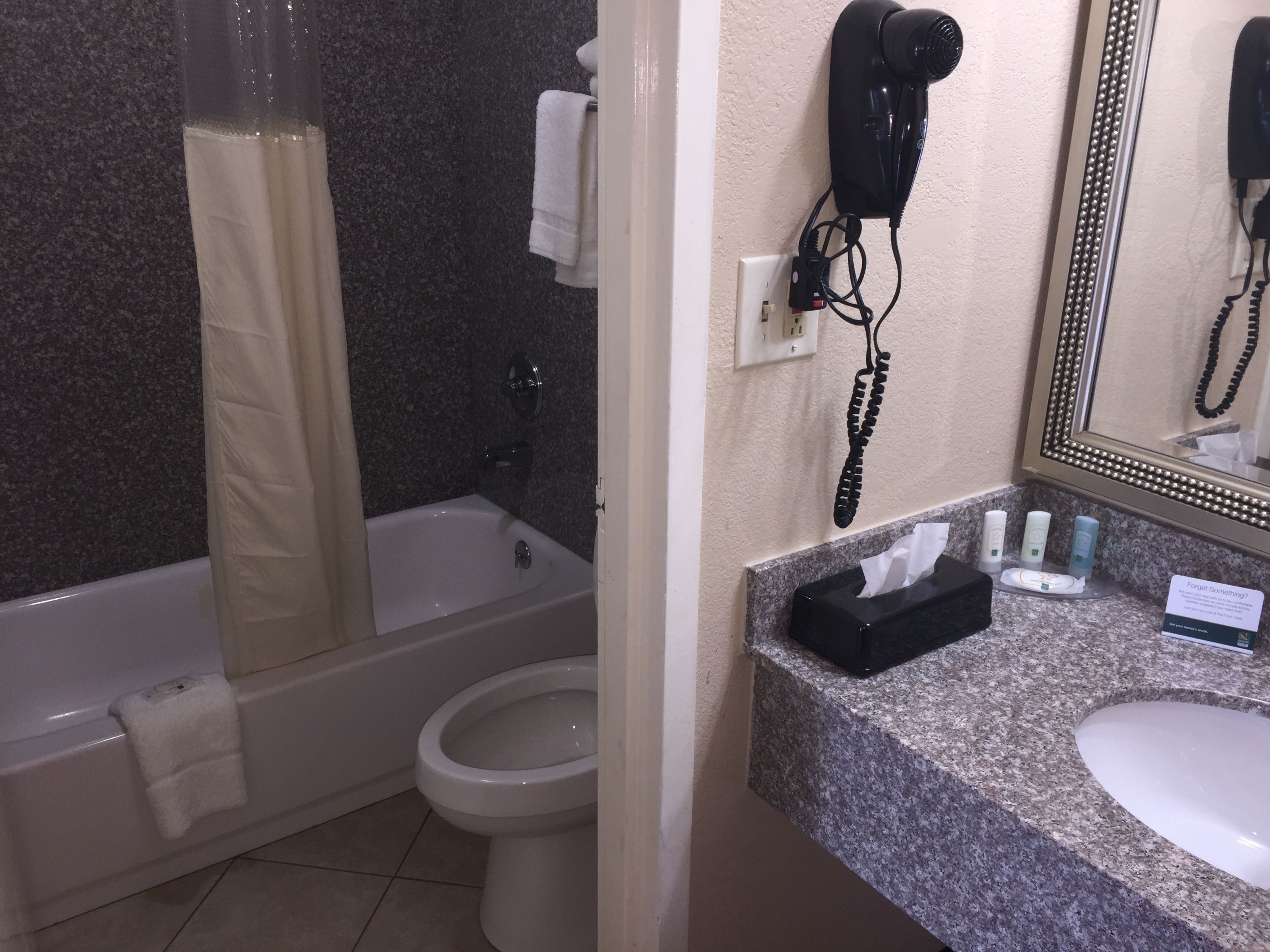 Ein Badezimmer mit Badewanne, Toilette und Waschbecken. Ein Fön ist an der Wand angebracht und auf der Ablage liegt eine Packung Taschentücher.