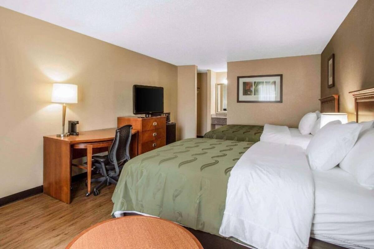 A hotel room with a bed, a desk with a chair, a television, and a lamp.