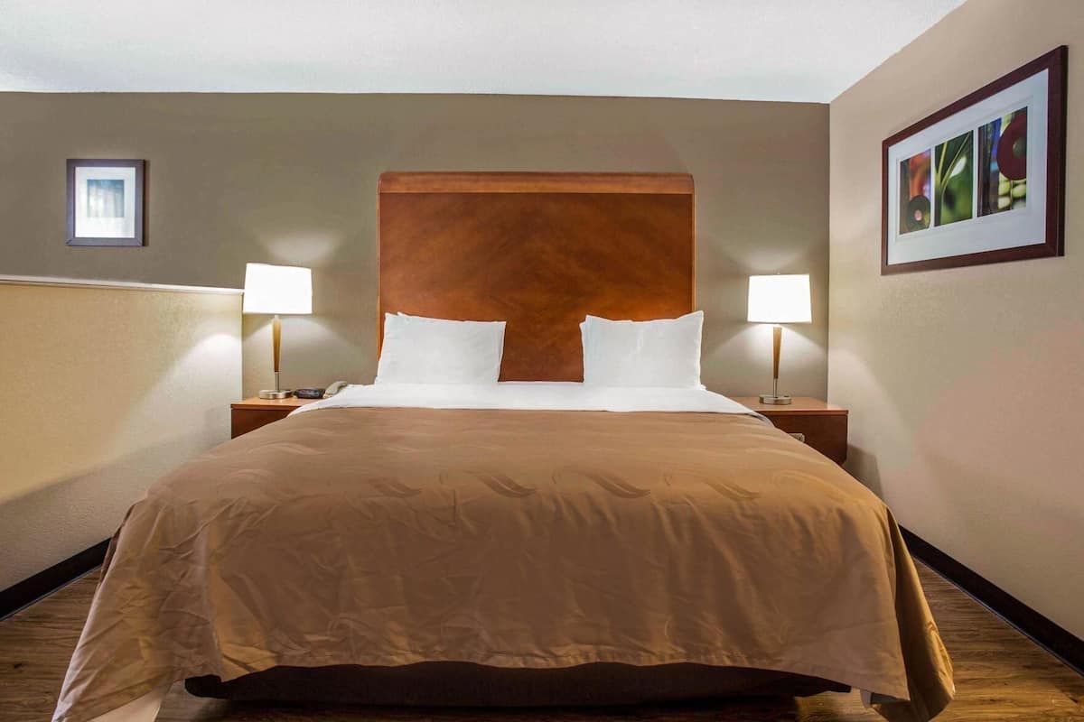 A hotel room with a large bed, two bedside lamps, a wooden headboard, and a framed picture on the wall.