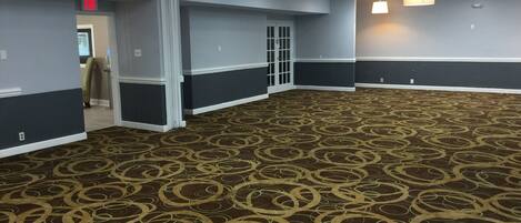 A spacious hallway with patterned carpet, a door with a glass panel, and a red exit sign.