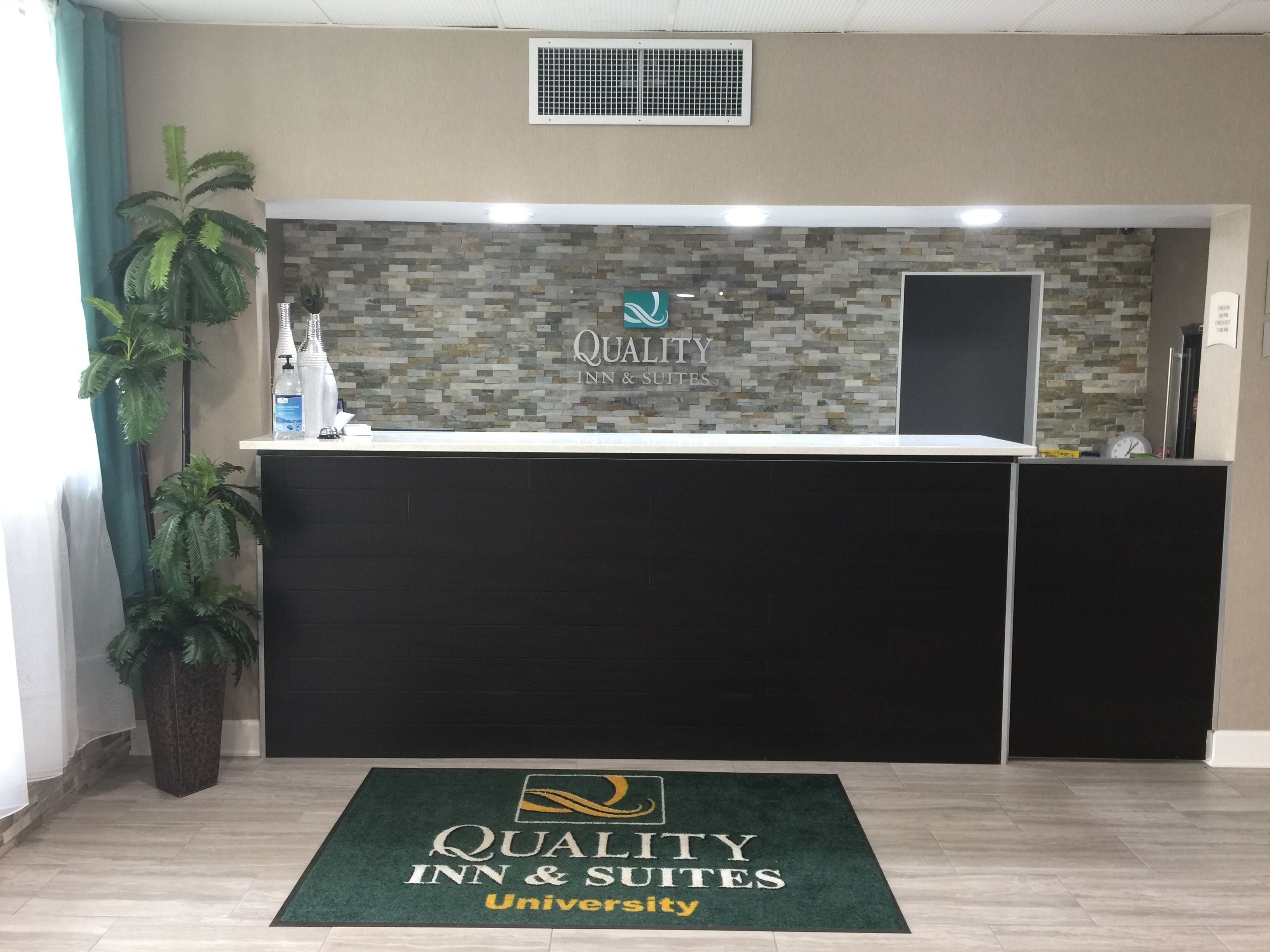 A reception desk with a mosaic tile wall, a logo, and a green mat with the hotel name.