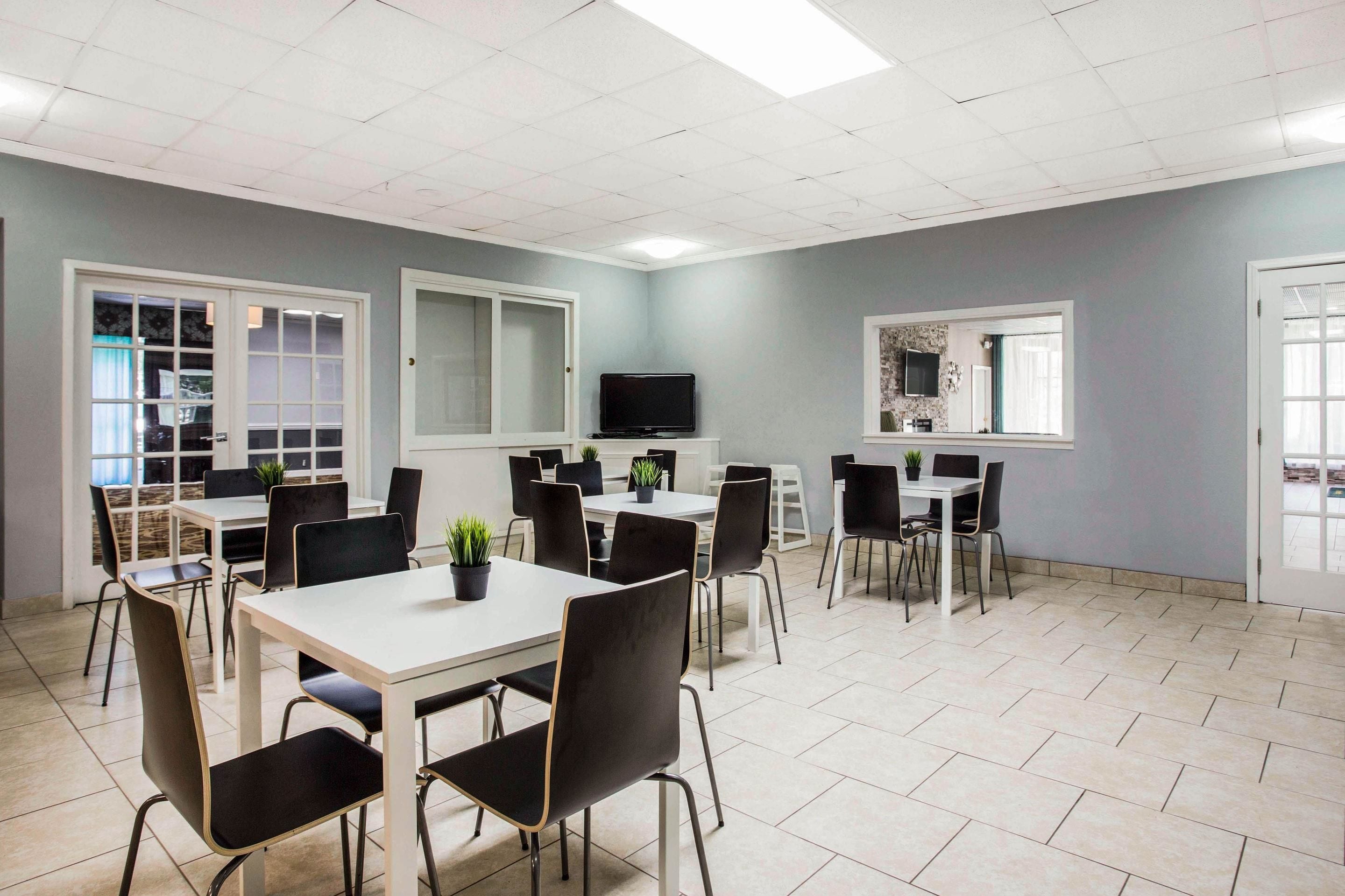A spacious room with multiple tables and chairs, a flat-screen TV, and large windows.