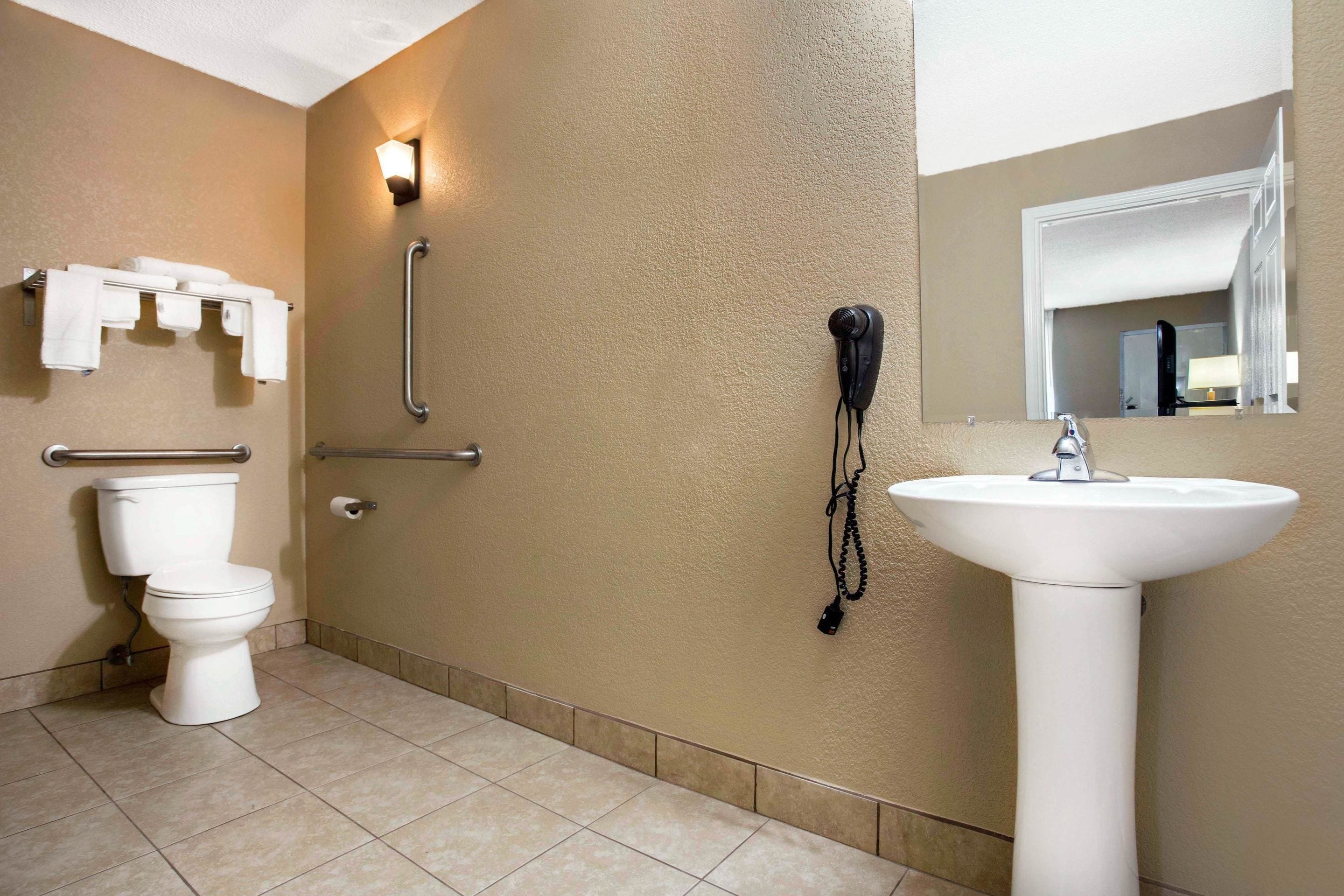 Un baño con inodoro, lavamanos, barra de apoyo y teléfono instalado en la pared.