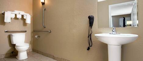 Un baño con inodoro, lavamanos, barra de apoyo y teléfono instalado en la pared.