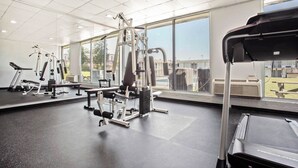 Ein Fitnessstudio mit unterschiedlichen Trainingsgeräten, großen Fenstern und einem Laufband.