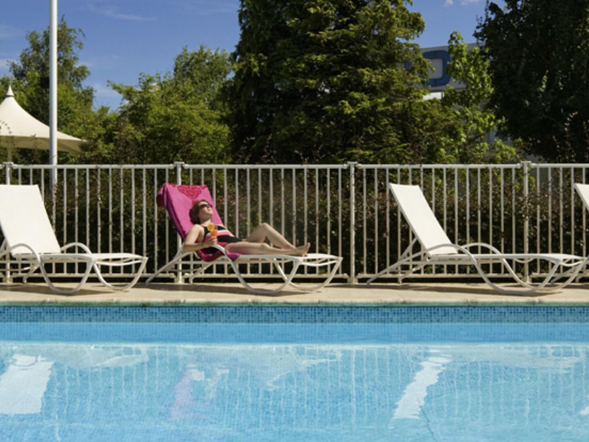 A swimming pool with lounge chairs and a person relaxing on one of them.