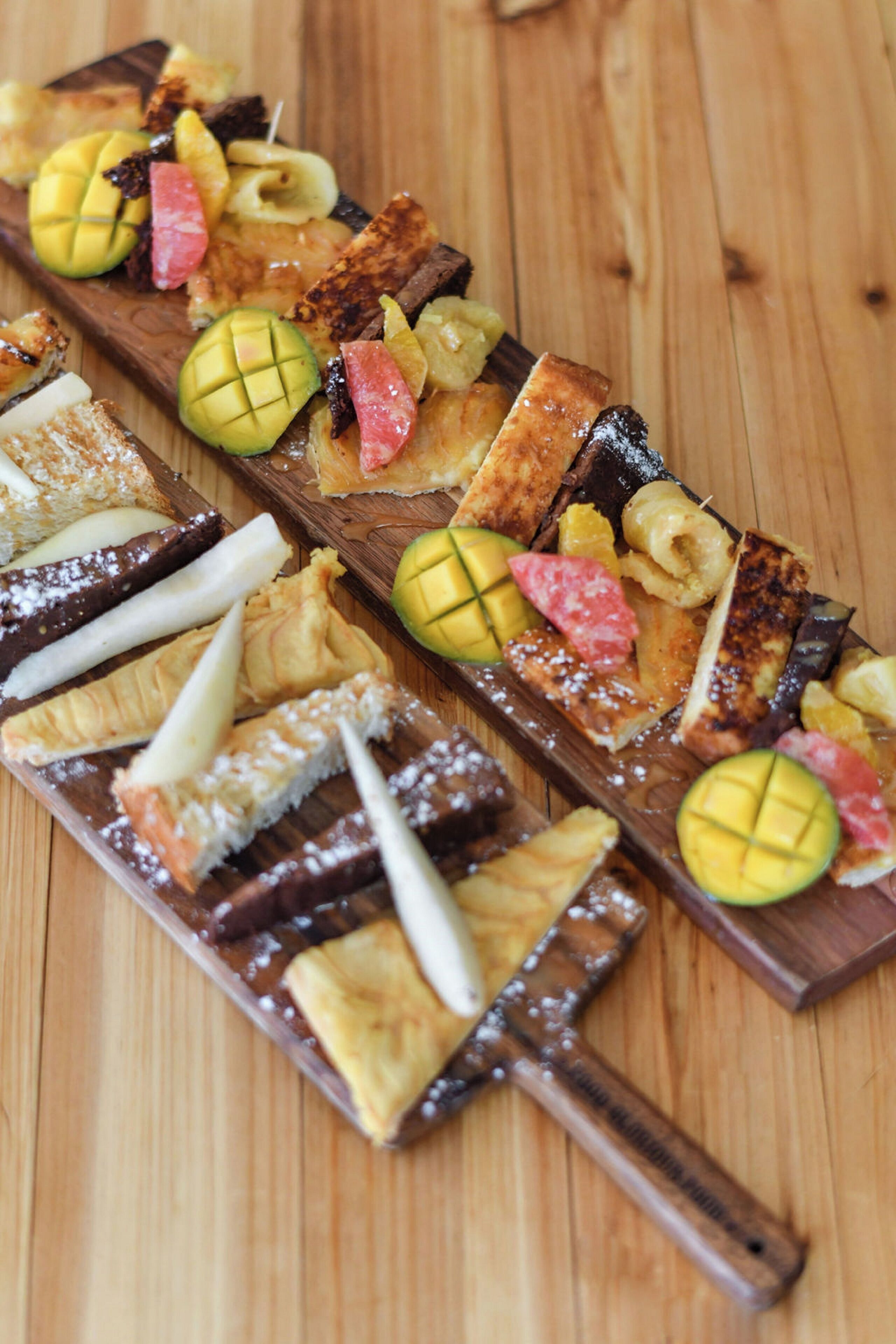 A wooden serving board with various food items, including slices of bread, fruit, and chocolate pieces.