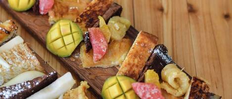 A wooden serving board with various food items, including slices of bread, fruit, and chocolate pieces.
