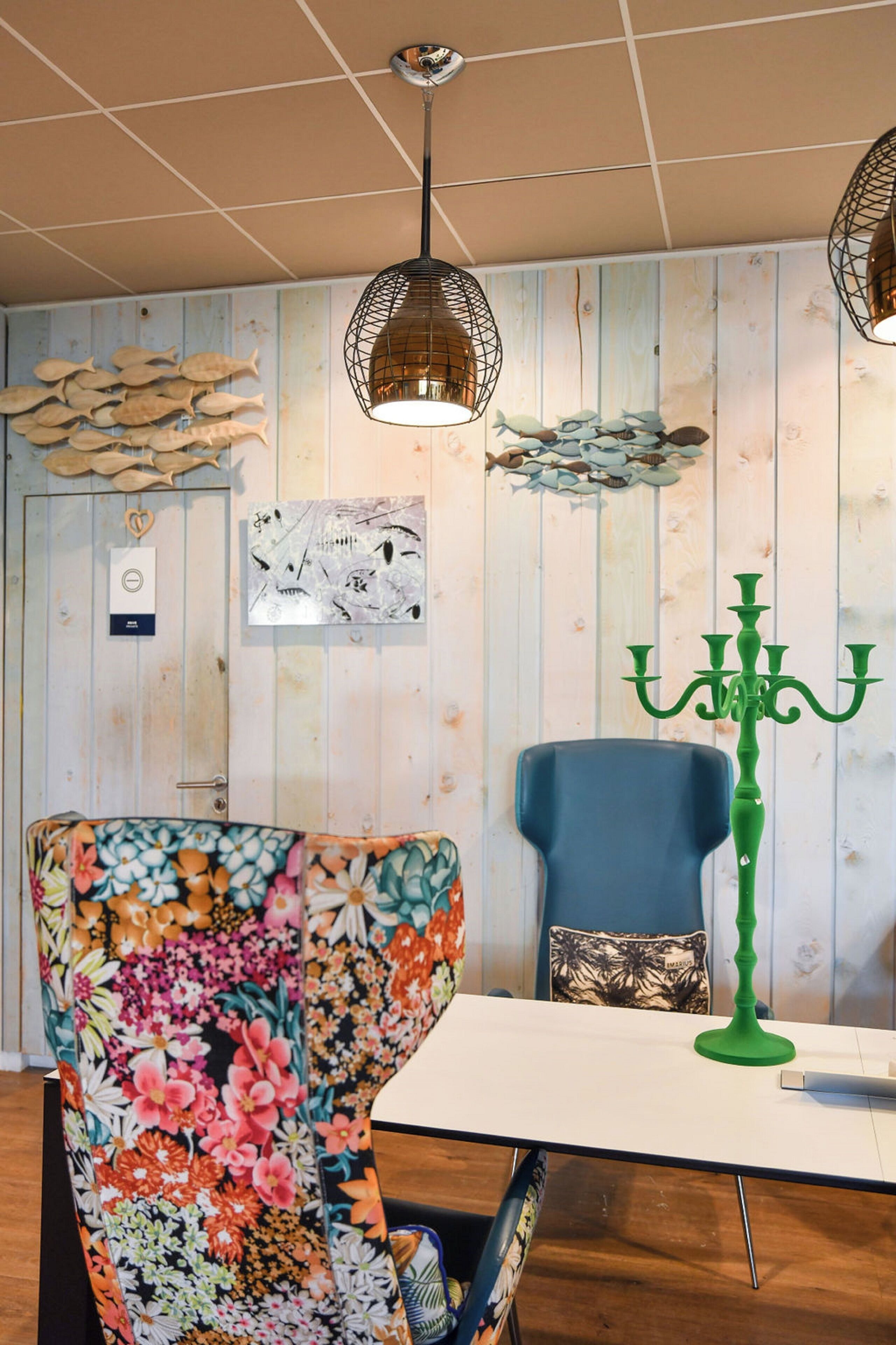 A room with a floral-patterned armchair, a blue chair, a white table, and a green candelabra.