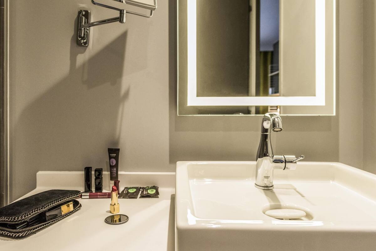 Une salle de bain avec un lavabo blanc, un miroir et des articles de toilette posés sur le comptoir.