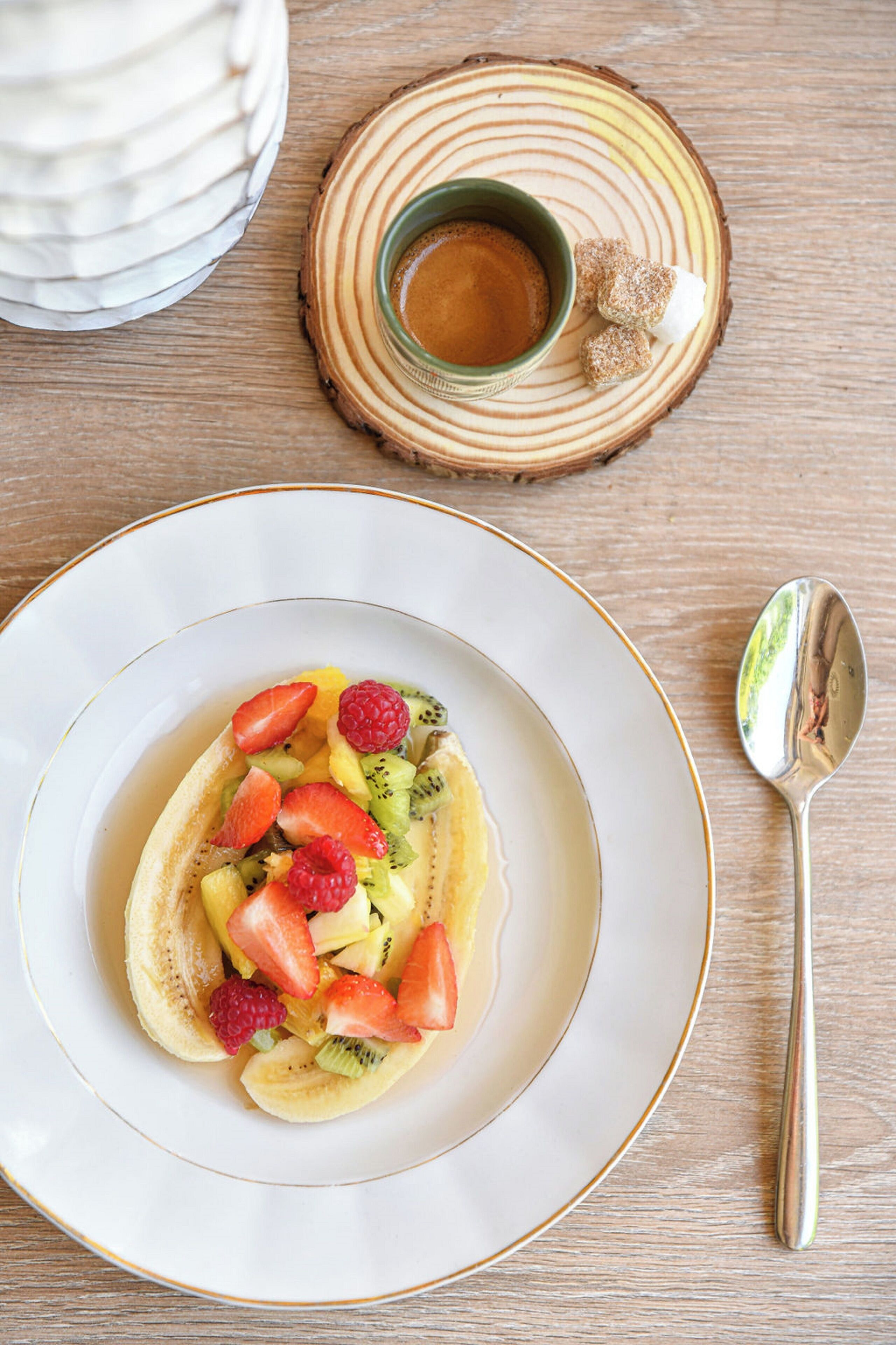 Een fruitsalade met aardbeien, kiwi en frambozen op een wit bord.