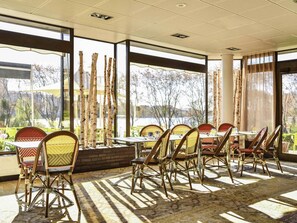 A dining area with tables and chairs, large windows, and a view of trees and a body of water. - Novotel Paris Créteil Le Lac (Creteil)