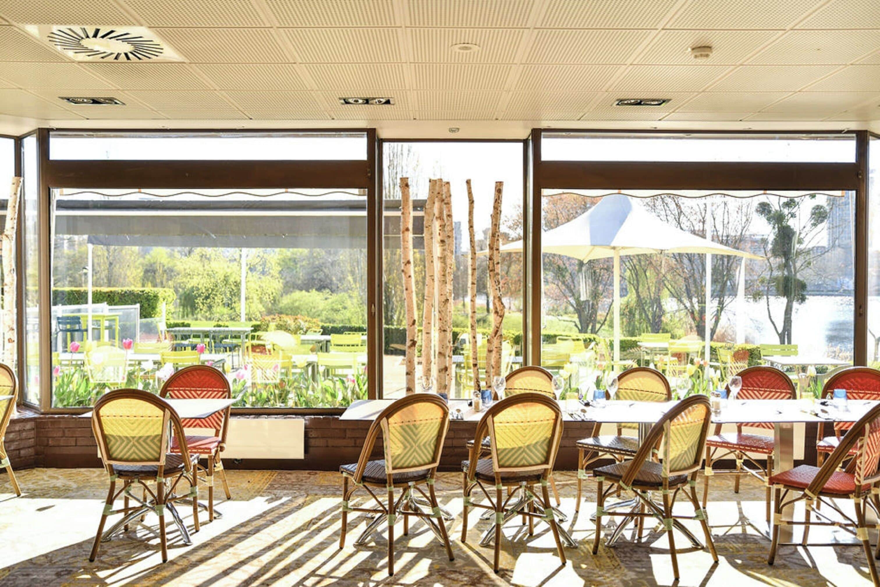 An indoor dining area with large windows, wicker chairs, and a table set for six.