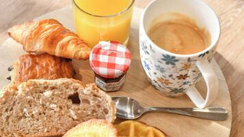Une assiette de petit-déjeuner avec des croissants, du pain, une gaufre, un verre de jus d’orange et une tasse de café, le tout posé sur une table en bois.