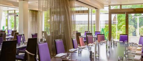 A conference room with round tables, purple chairs, and large windows with curtains.