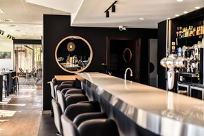 Un espace bar moderne doté d’un long comptoir, de tabourets de bar et d’un mur recouvert de miroirs.