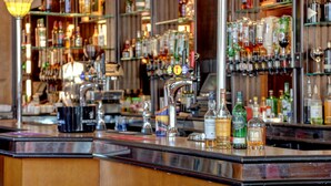 A bar with multiple shelves of liquor bottles, a tap, and a coffee machine.