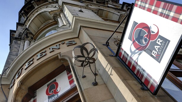 A building facade with the sign "Queen's Bar" and a large advertisement for "Bar & Grill."