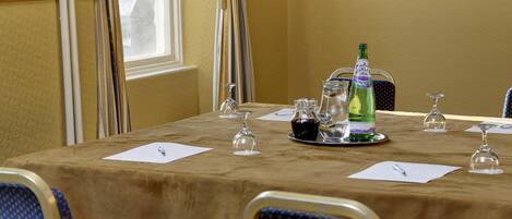 Une salle de conférence avec une table préparée pour une réunion, comprenant une bouteille d’eau, des verres à vin et un bloc-notes.