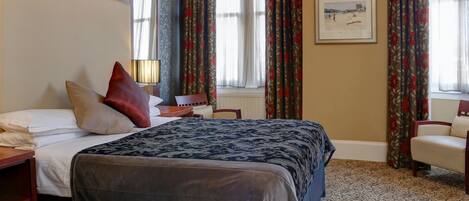 Een hotelkamer met een groot bed, een nachtkastje, een stoel en een raam met gordijnen.