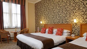 A hotel room with two beds, a wooden headboard, a patterned wallpaper, and a window with curtains.