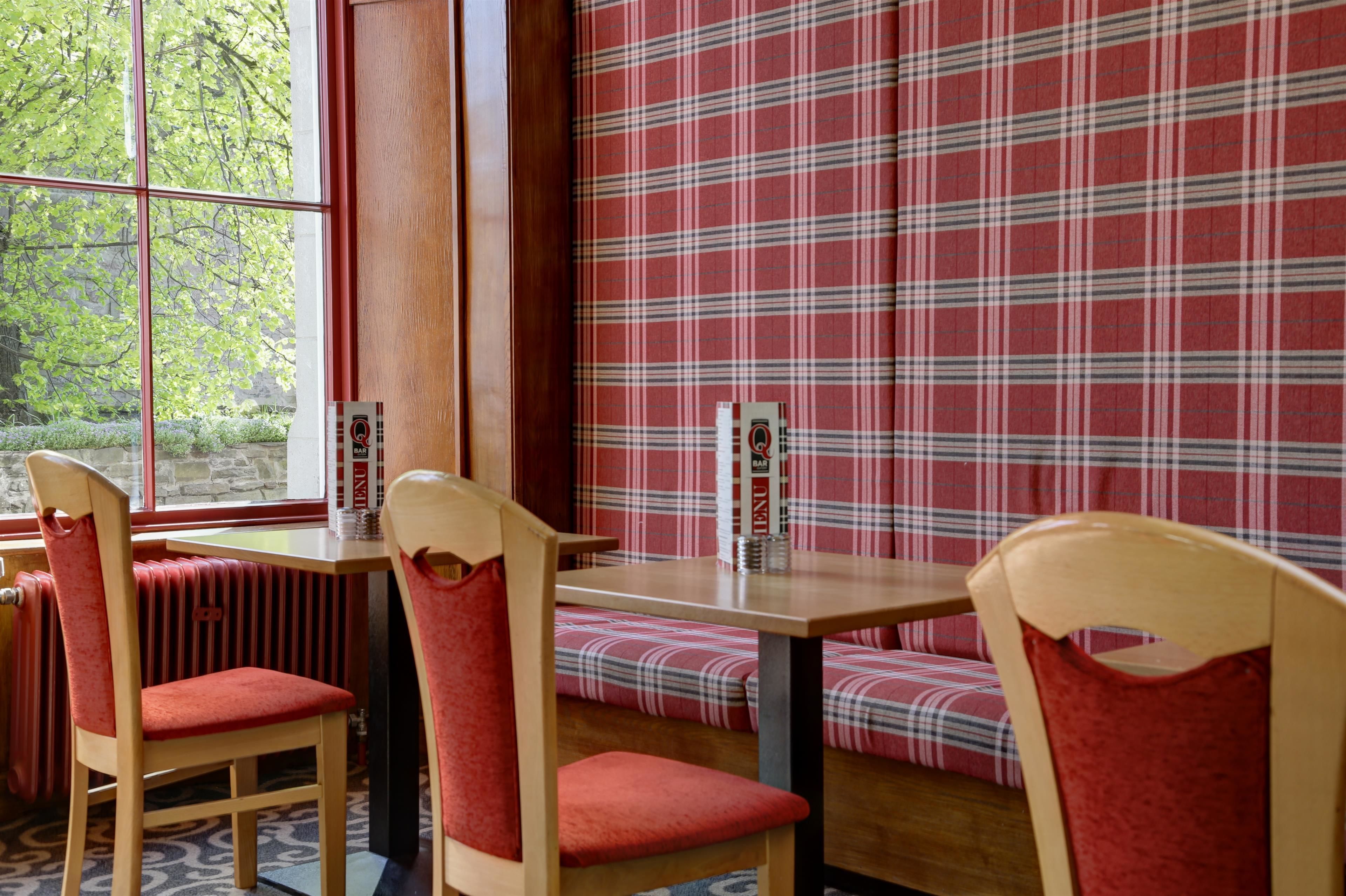 A dining area with wooden chairs and benches, a table, and a window with a view of greenery.