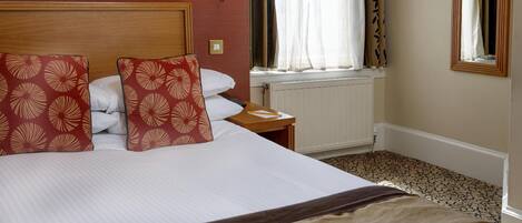 A hotel room with a large bed, a nightstand, a lamp, a window with curtains, and a radiator.