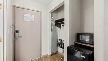 Habitación de hotel con puerta, un refrigerador pequeño, microondas y un perchero con toallas.