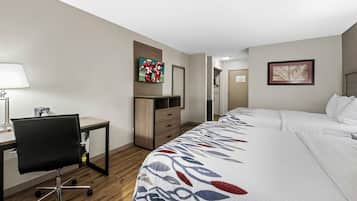 A hotel room with a bed, desk, chair, and a television on the wall.