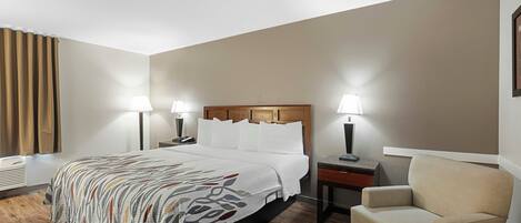 A hotel room with a bed, bedside lamps, a chair, a nightstand, and a wall-mounted air conditioner.