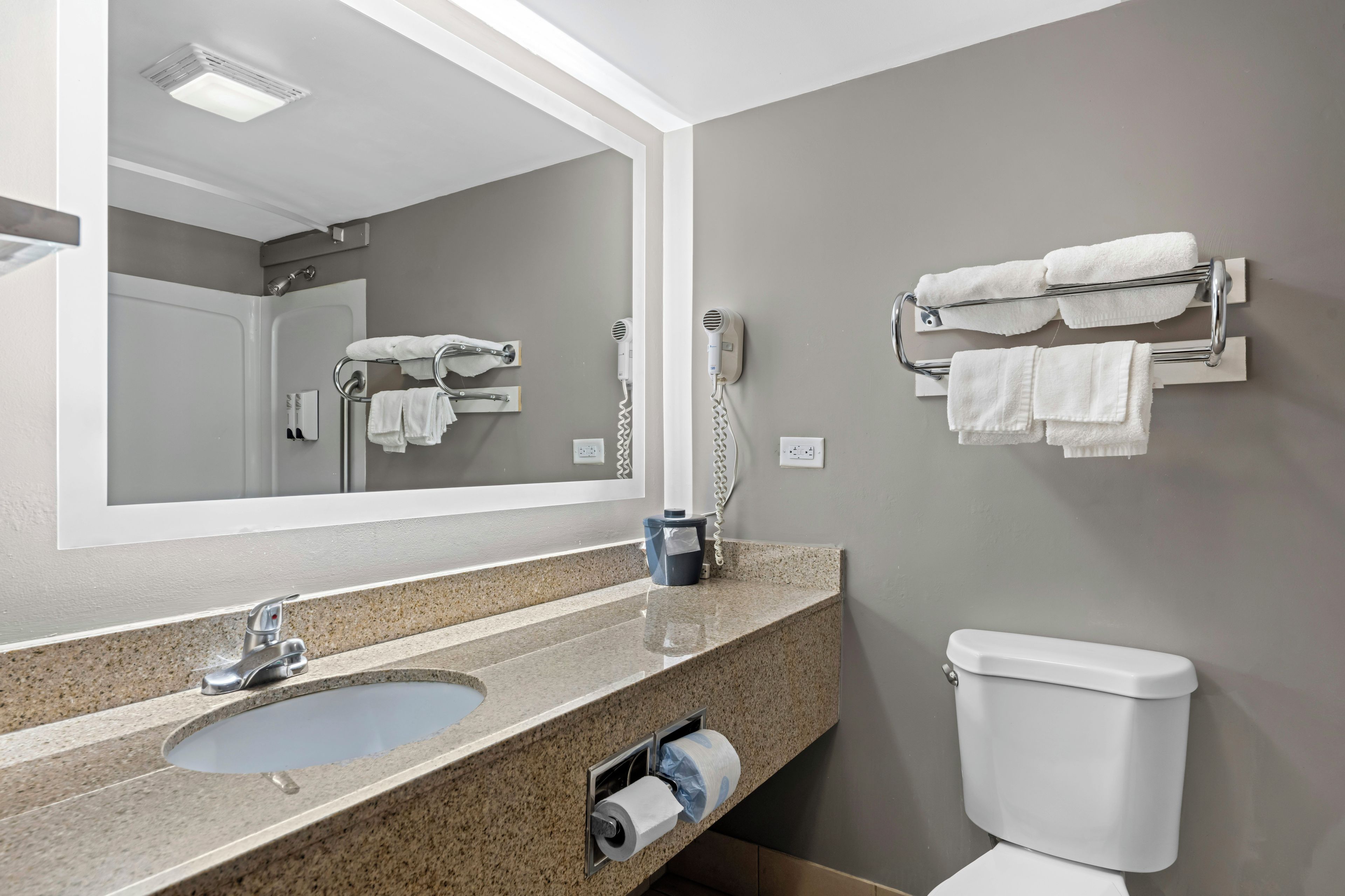 A bathroom with a sink, mirror, towel rack, toilet, and a hairdryer.