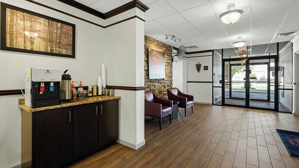 A reception area with a coffee machine, seating, a stone accent wall, and a view through the door. - Red Roof Inn Gurnee - Waukegan (Waukegan)