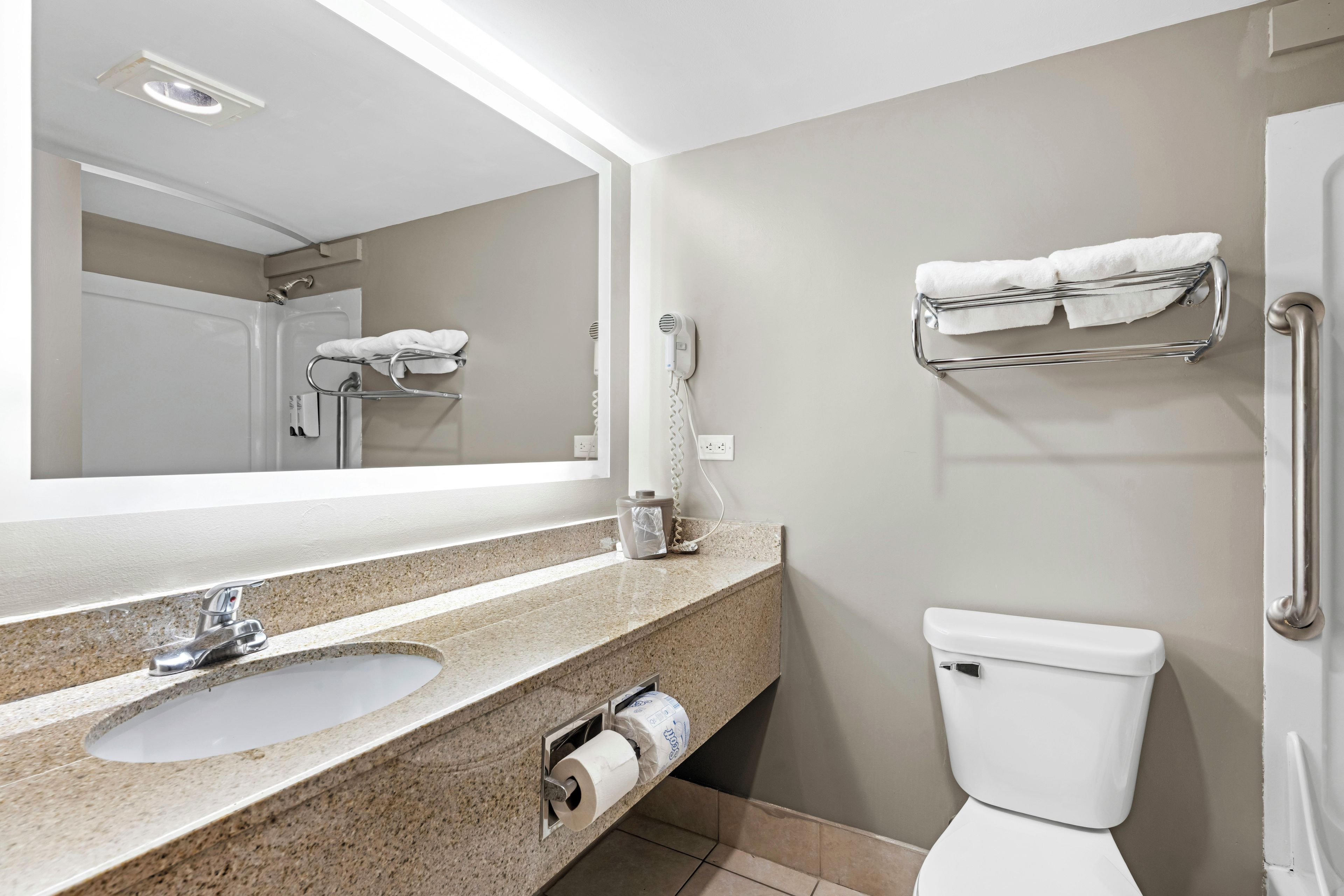 Ein Badezimmer mit Waschbecken, Spiegel, Handtuchhalter, Toilette und einem Fön.