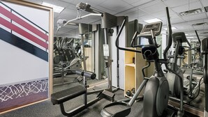 A gym with exercise equipment, a mirrored wall, and a staircase with red and white stripes. - Red Roof Inn Gurnee - Waukegan (Waukegan)