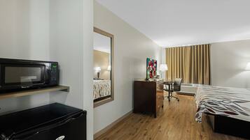 A hotel room with a bed, a desk, a chair, a desk lamp, a television, a microwave, and a dresser.
