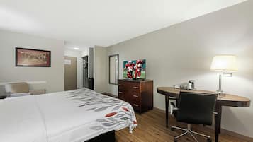 A hotel room with a bed, a desk, a chair, a television, and a lamp.